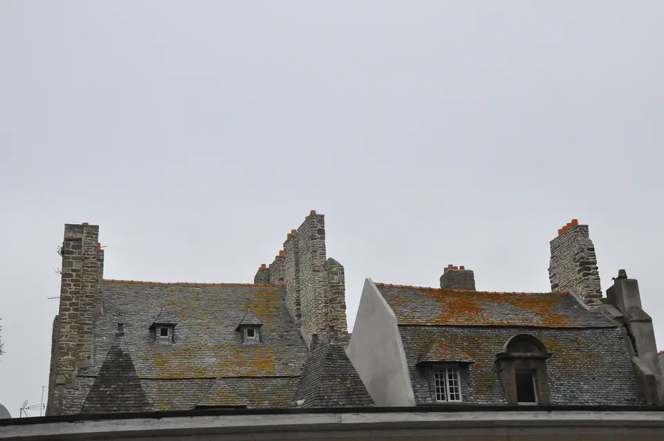 Massives souches de cheminées en granit et toits d'ardoise à lucarnes à Saint-Malo.